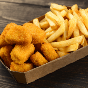 Wild Ireland - A cardboard container filled with golden-brown breaded chicken nuggets on one side and thick-cut French fries on the other, placed on a dark wooden surface.